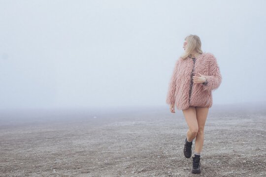 Stylish person in pink fur coat and sunglasses outdoors on a foggy day