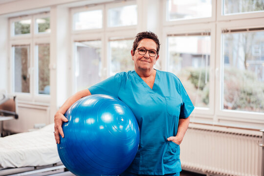 Physiotherapist in scrubs with exercise ball in physiotherapy rehabilitation room