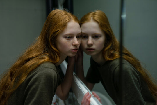 Red haired woman with freckles leaning against mirror in old building