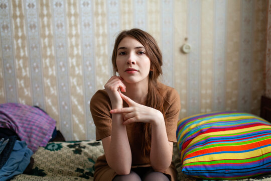 Woman in dress sitting thoughtfully on bed in old house interior