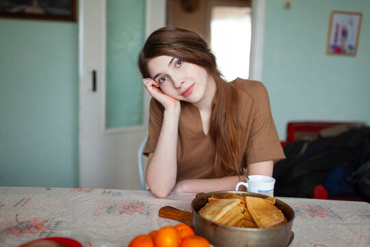 Woman in brown dress relaxing at kitchen table with pancakes
