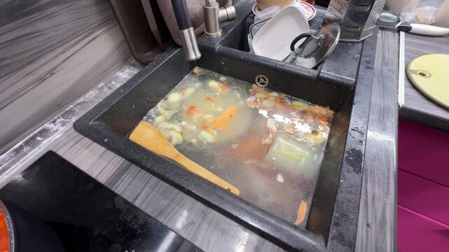 Overflowing water from a blocked sink floods the kitchen floor, threatening cabinets, baseboards, and appliances with damage from food waste and standing water.