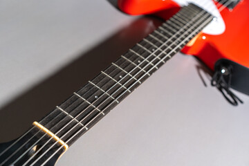 Close-up of a red electric guitar showing the fretboard with metal frets and dot inlays, strings running along the neck, part of the body with white pickguard, and attached black strap.