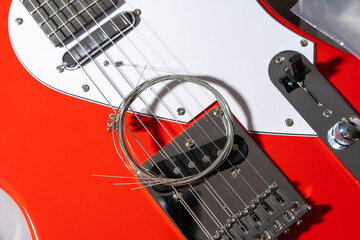 Close-up of a red electric guitar with white pickguard, chrome hardware, dual pickups, bridge saddles, and a coiled set of new metallic strings resting on the body.