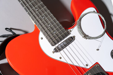 Close-up of a red electric guitar with white pickguard, dark fretboard, metal frets, dot inlays, black strap, and a coiled set of new metallic strings resting on the body.