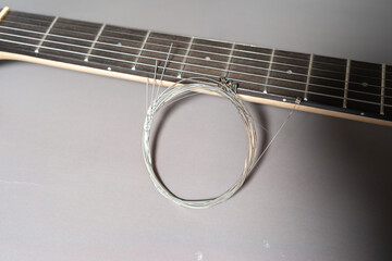 Close-up of a guitar neck with dark fretboard, metal frets, dot inlays, and a coiled set of new metallic strings resting across the frets.