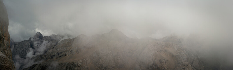 Moody panoramic view of rugged Dolomites peaks disappearing into low clouds near Punta Penia summit...