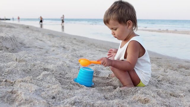 Boy playing with toys on the beach building beads and turrets smiling at someone behind the scenes on summer vacation