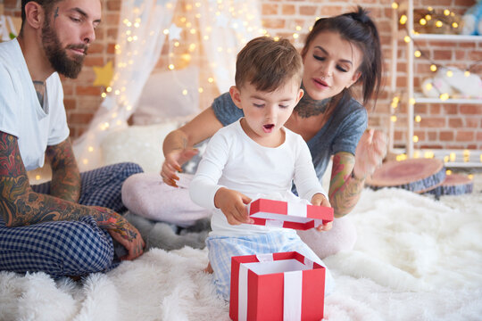 Surprised boy opening Christmas present with his parents in bed