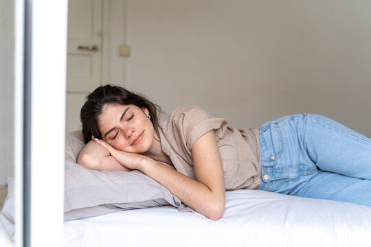 Smiling young woman lying on bed with closed eyes