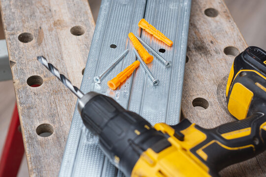 Cordless drill with drill bit, plastic wall plugs and metal screws on galvanized metal profile. Construction and installation concept for renovation, drywall mounting and home improvement projects.