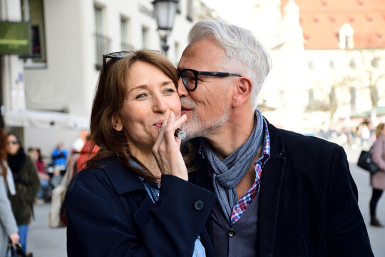 Mature couple walking in the city, woman smoking electronic cigarette