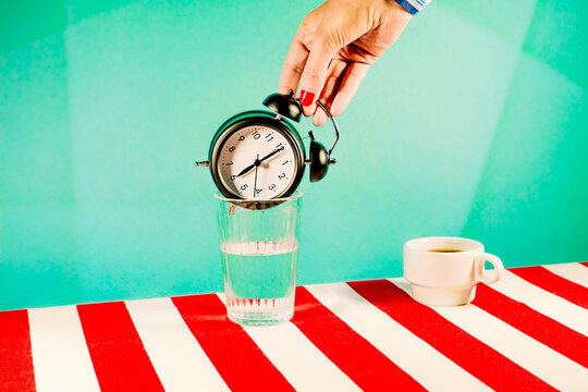 Hand of woman trying to put alarm clock inside glass of water