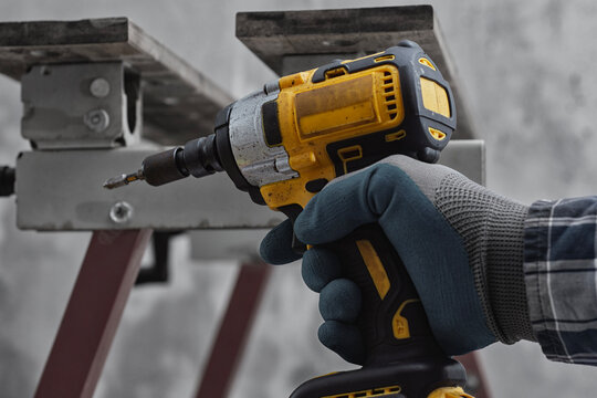Worker using cordless impact driver to fasten metal structure. Professional installation process at construction site. Concept of industrial work, renovation, engineering and building assembly.