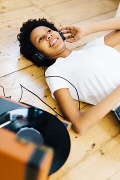 Young woman at home listening vinyl records, lying on ground