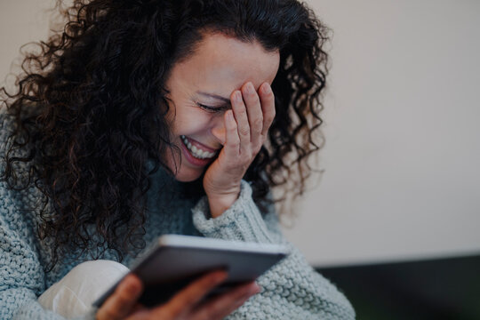 Woman sitting at home, using digital tablet, laughing