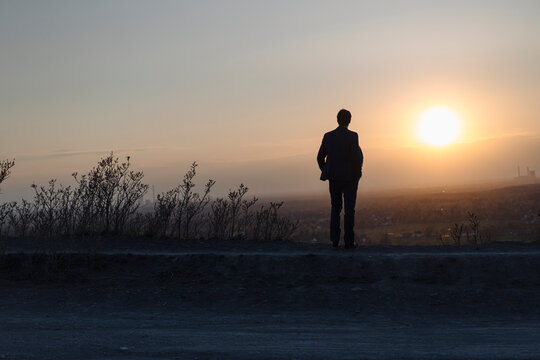Mature businessman standing on a disused mine tip at sunset looking at view