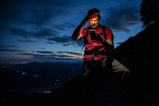 Male hiker checking map over smart phone while standing on mountain at night, Orobie, Lecco, Italy