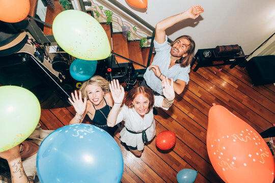 Male and female friends dancing with colorful balloons during party at home
