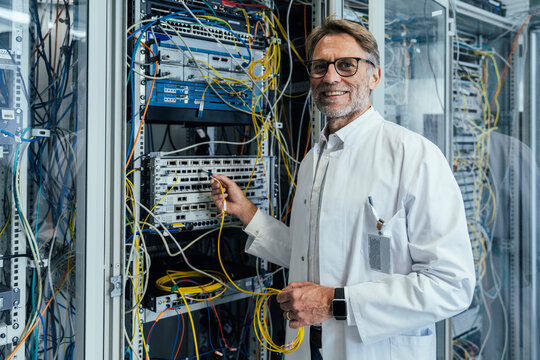 Smiling mature man plugging transceiver on fiber optic cable in data center