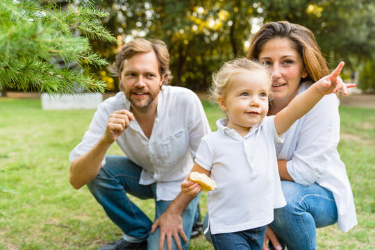 Parents with little daughter pointing her finger on a meadow