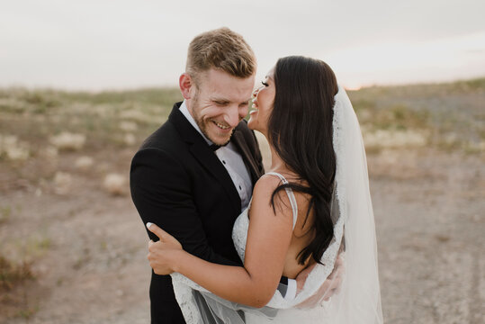 Happy groom embracing bride while standing in field against sky