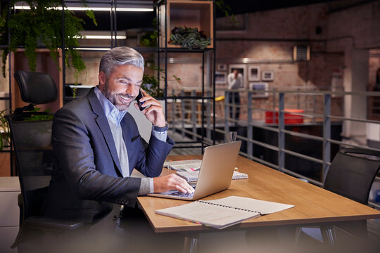 Mature businessman working in modern office, using laptop while talking on the phone