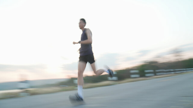 Panning shot of energetic runner guy jogging along highway with speed and high performance during evening copy space background