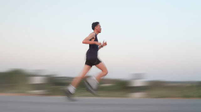 Athletic runnersMotion blur side view of young man running fast on asphalt road outdoor during sunset for healthy lifestyle concept in motion blur, representing speed and active lifestyle