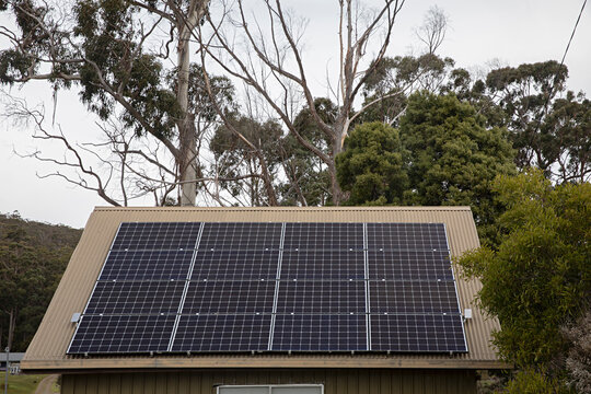 Modern solar panels installed on a sloped roof of a small building surrounded by trees in Australia