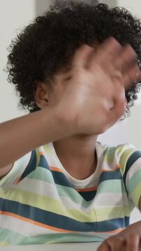 Vertical video: Waving boy in striped tee after off-camera cue, smiling, fiddling at table with art