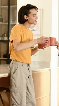 Vertical video: Accepting man in orange tee taking mug from right side hand, chatting at kitchen