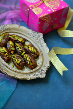 Pistachio-stuffed dates served in an ornamental plate, placed along with a gift box. Eid celebrations, gift and food photo background.