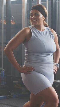 Vertical video: After lunge woman stepping and standing in gym, wearing blue set, power rack behind