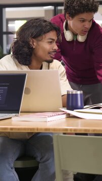 Vertical video: Approaching male with headphones leaning at lounge pointing at laptop for study
