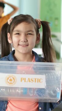 Vertical video: Displaying girl wearing denim reacting to camera at class, holding PLASTIC box