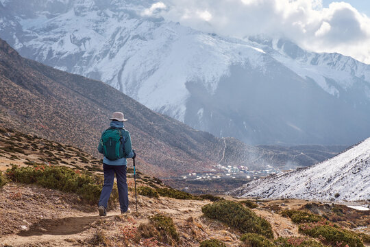 Happy woman trekker with backpack walks on mountain path towards Dingboche village, surrounded by snow-capped Himalayan peaks during Everest Base Camp trek, Nepal.