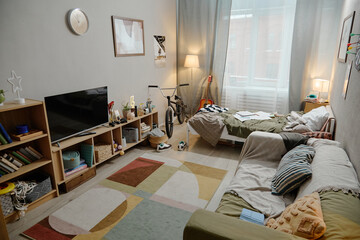 Cozy teenagers bedroom interior featuring single bed with rumpled bedding, bicycle standing near window, guitar leaning against wall, and wooden shelving with television and decor © Seventyfour