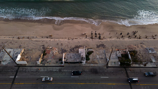 Aerial view of the rugged coastline meeting remnants of buildings and a road bustling with cars, Malibu, California, United States.