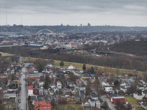 Aerial view of the cityscape unfolding under a muted sky, with the arched bridge and distant towers punctuating the horizon, Newport, Kentucky, United States.