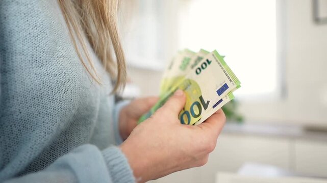 Blonde white woman counting euro notes in cozy kitchen, blue sweater, closeup hands sorting cash, mindful budgeting, cashflow tracking, personal finance content Blonde white woman counting euro notes 