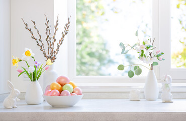 Naklejka premium Easter table decoration on springtime window background with colorful eggs, ceramic rabbits and fresh flowers