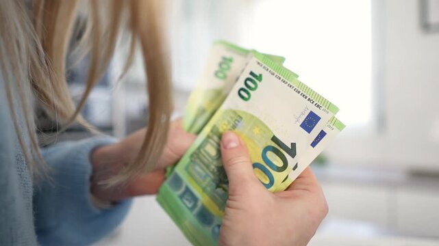 Blonde white woman counting euro notes in cozy kitchen, blue sweater, closeup hands sorting cash, mindful budgeting, cashflow tracking, personal finance content Blonde white woman counting euro notes 