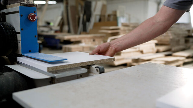 Worker processing a laminated particle board panel on industrial machinery in a furniture workshop.