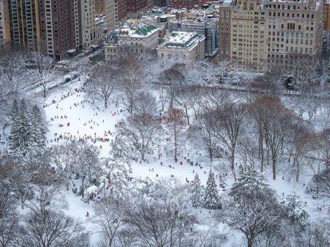 Aerial view of snow-blanketed Central Park filled with tiny figures enjoying a winter wonderland moment amidst the towering buildings, Manhattan, New York, United States.
