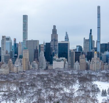 Aerial view of Central Park's snowy blanket contrasting with the towering skyscrapers of Billionaires' Row piercing the overcast sky, Manhattan, New York, United States.