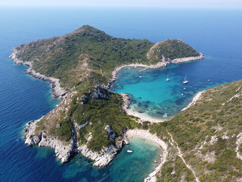 Aerial view of a lush island embraced by turquoise waters, revealing hidden beaches and rocky outcrops in a dance of blue and green, Corfu, Corfu, Greece.