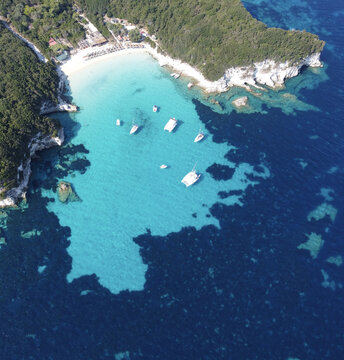 Aerial view of boats bobbing in the turquoise Ionian Sea, cradled by the verdant hills and pale cliffs of Corfu's coastline, Corfu, Corfu, Greece.