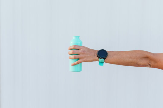 Arm holding a turquoise reusable water bottle and wearing a smartwatch, hydration and fitness concept with copy space.