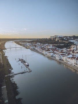 Aerial view of the tranquil Sado River reflecting the sky, embraced by the white buildings and terracotta roofs of the city, Alcacer do Sal, Setubal, Portugal.